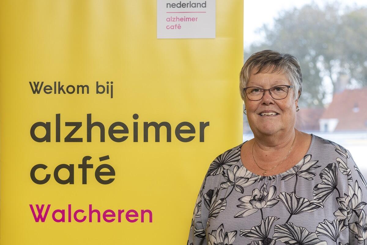Foto van Jessy Benne bij een banner van het Alzheimercafé, foto gemaakt door Anda van Riet Fotografie